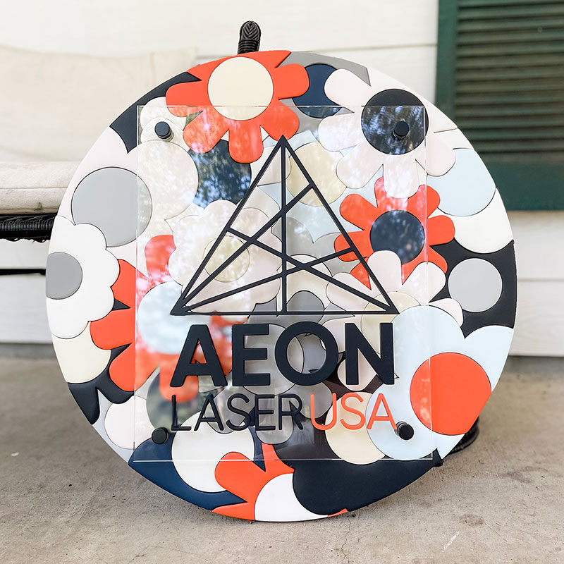 round wooden sign made of orange, blue, and white flowers with a prism and kendrasunderland logo on top