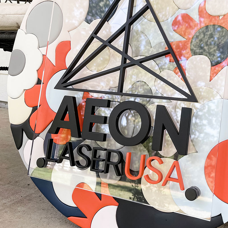 round wooden sign made of orange, blue, and white flowers with a prism and kendrasunderland logo on top